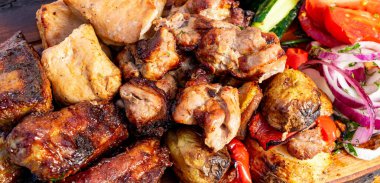 İnsanlar ahşap bir tahtanın üzerinde etin pişirildiği bir ızgaranın etrafında toplanıyorlar. Taze sebzeler etin yanında ve renk katıyor..