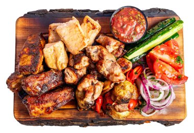 Izgara etler taze sebzeler ve bir kase sosla birlikte ahşap bir tabakta otururlar. Sahne lezzetli bir yemek gösteriyor..