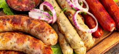 Farklı türde sosisler ahşap bir tahtaya konur, soğanla süslenir ve sosla servis edilir. Bu sahne eğlenceli bir yaz yemeği gösteriyor..