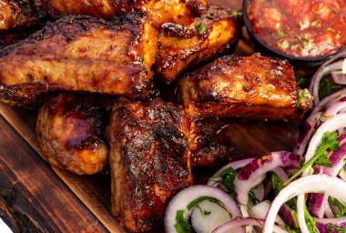 Pişmiş et parçaları bir yaz etkinliği sırasında ahşap bir tabakta sos ve taze sebzelerle servis edilir..