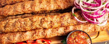 Kebaplar ahşap bir tahtaya konur. Sos, taze soğan ve dilimlenmiş biberle birlikte. Bu sahnede yemek zevke hazır..