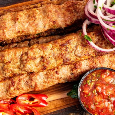 Izgara kebaplar ahşap bir tabağa konur. Yanında da kırmızı soğan, dilimlenmiş biber ve bir kase salsa sosu..