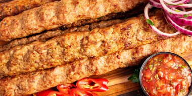 Izgara kebaplar sosun, dilimlenmiş kırmızı soğanın ve markette taze kırmızı biberin yanında ahşap bir tahtada oturur..