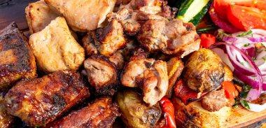 İnsanlar ahşap bir tahtanın üzerinde etin pişirildiği bir ızgaranın etrafında toplanıyorlar. Taze sebzeler etin yanında ve renk katıyor..