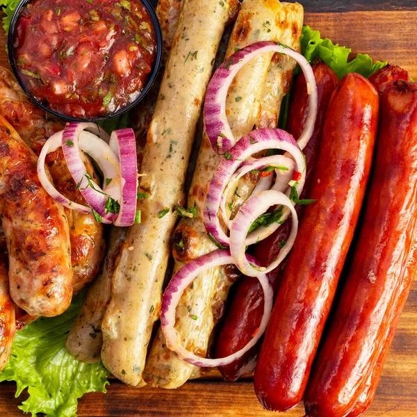 Farklı türde sosisler ve sosisler ahşap bir tahta üzerinde kırmızı soğan ve bir kase sos ile düzenlenir..