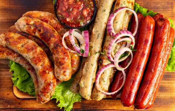 Sosisler ahşap bir tahtada, biraz marul ve bir kase salsa ile düzenlenir. Soğanlar yemeğe tat katar..