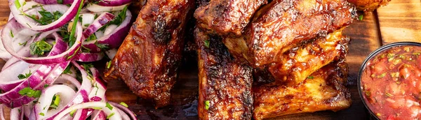 Barbekü kaburgaları dilimlenmiş soğan ve küçük bir kase sosla ahşap bir tabakta servis edilir. Bu sahne bir yaz toplantısında yiyecekleri gösteriyor..