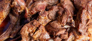 Et parçaları ızgarada pişirilir ve ahşap bir tahtada sunulur. Arkadaşlar barbekü sırasında birlikte yemek yerler..