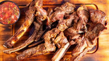 Et ahşap bir tahtanın üzerinde, küçük bir kase sosla servis edilir. Dekorasyon, ızgara yemek hazırlama üzerine odaklandığını gösteriyor..