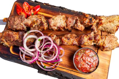 Izgara et şişleri dilimlenmiş soğan ve bir kase sosla ahşap bir kesme tahtasının üzerine konur. Kırmızı biber yemeğe renk katar..