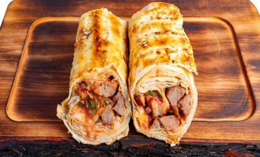 Et ve sosla dolu iki paket mutfaktaki ahşap bir tahtanın üzerinde duruyor. Sargılar ızgara ve lezzetli görünüyor..