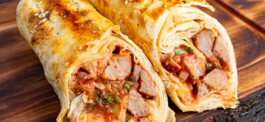 İçerideki et ve sosu göstermek için iki burrito ikiye bölünür ve ahşap bir masaya servis edilir..