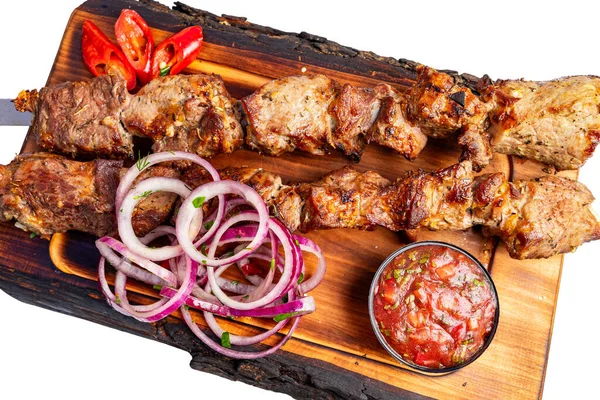 Izgara et şişleri dilimlenmiş soğan ve bir kase sosla ahşap bir kesme tahtasının üzerine konur. Kırmızı biber yemeğe renk katar..