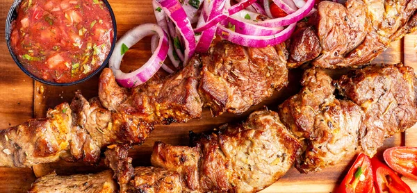 Izgara et, dilimlenmiş soğan ve bir kase salsa ile ahşap bir tahtada sergilenir. Ayarlar sıradan bir yemek saati olduğunu gösteriyor..