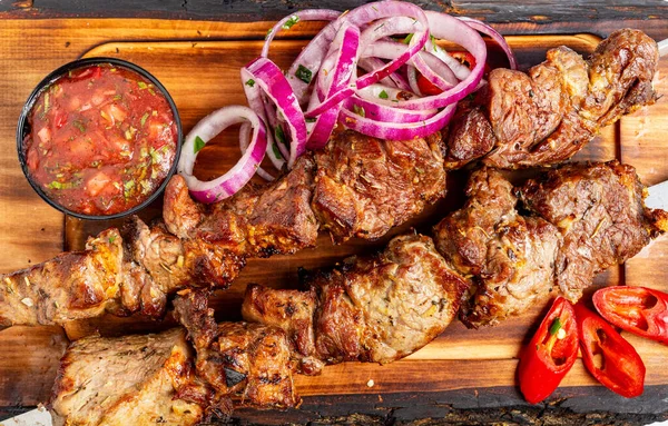 Ahşap bir tabakta, akşamları toplanırken, yanında salsa sosu ve dilimlenmiş soğanla ızgara et olur..