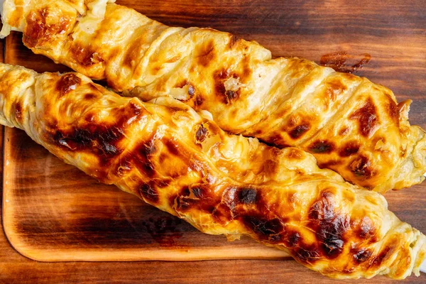 İki fırınlanmış hamur işi tahta bir tahtanın üzerinde, altın kahverengi bir kabuk ve pul pul bir doku gösteriyor..