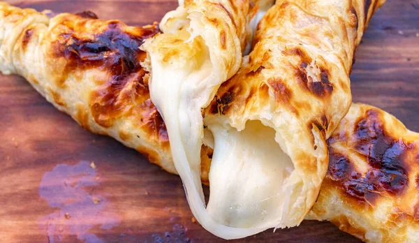 Peynirle dolu hamur işleri ahşap bir tahtaya oturup içeriden sızan erimiş peynirleri gösterir..