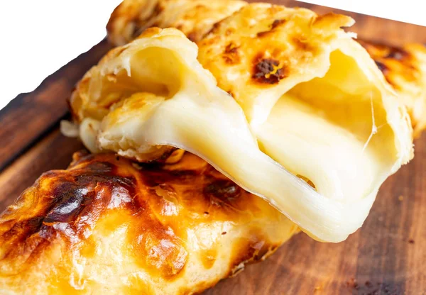 Bir peynirli hamur işi ahşap bir tahtanın üzerinde altın hamurla duruyor. Dolgu sarkık ve eriyor, zenginliği gösteriyor..