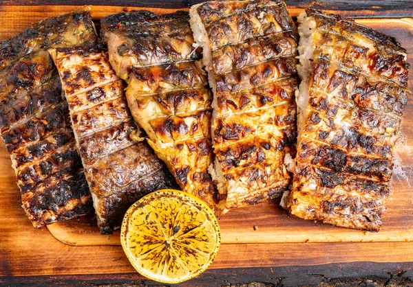 Balık filetoları güzel işaretlenene kadar ızgara yapılır ve ızgara limon dilimleriyle ahşap bir tahtada servis edilir..