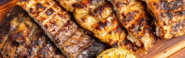 Farklı türde ızgara balık ahşap bir tabakta düzenlenir. Balıkların yanında bir dilim limon var. Bu bir restoranda servis edilir..