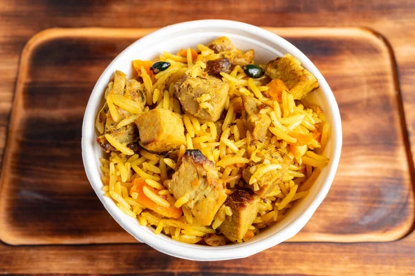 Bir kasede pişmiş et ve sebze parçalarıyla karışık sarı pirinç bulunur. Ahşap zemin ile ayarlar basit..