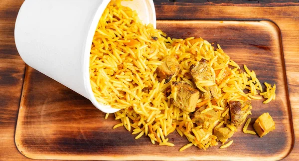 Biryani pirinci beyaz bir konteynırdan ahşap bir tahtanın üzerine dökülür. Yemekler dağınık ve renkli..