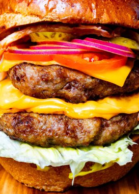 Bir duble çizburger ahşap bir yüzeyde marul, domates, soğan ve peynirle istiflenir..