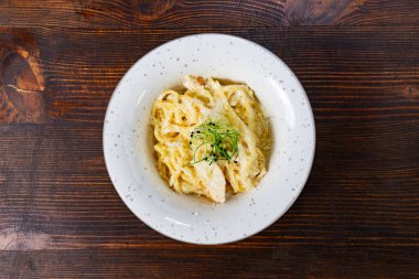 Kremalı makarnalı bir tabak ahşap bir masada oturur. Tabağın üzerinde yeşil bir garnitür var..