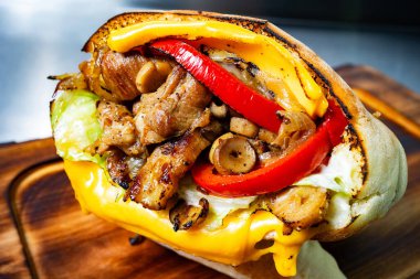 Tahta bir tahtada peynirli ızgara tavuk sandviçi, kırmızı biber ve marul sunulur. Taze ve lezzetli görünüyor..