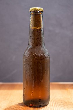 Bir şişe soğuk bira, bir damla buğulama ile taş duvar arka planında bir masanın üzerinde servis edilmek üzere.