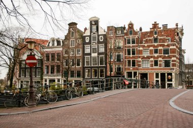 Amsterdam, Hollanda, 01-18-2008; Amsterdam 'da bir kanal üzerinde köprü, şehrin tipik evleri ve bulutlu ve gri bir günde merdivenlerin yanında demirlemiş bir tekne.