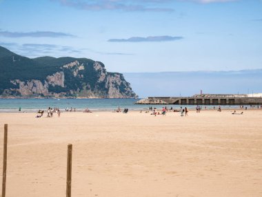 Laredo, Cantabria, İspanya; 08-17-2021: Laredo sahili manzarası, yazın keyfini çıkaran turistler, modern marinanın yanındaki kum ve deniz suyu ve arka plandaki Santona kayası