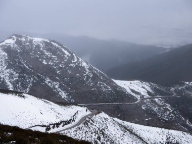 El Bierzo 'da dar, asfalt bir yol karla kaplı dağların yamaçlarının arasına tırmanıyor keskin, dolambaçlı eğriler ve arka planda kalın bir sis var.