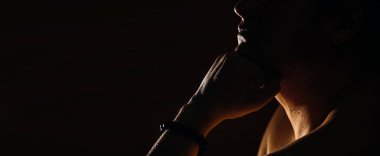 Gövdesi açık beyaz bir adam koyu bir arka planda, pankartta düşünceli bir şekilde oturur.