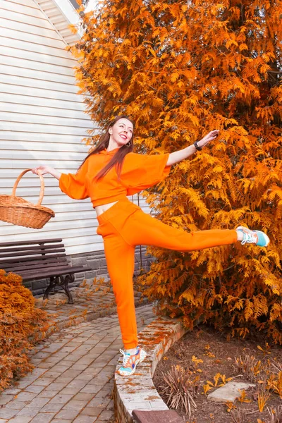 A girl in a jump in a bright orange suit against the background of autumn foliage