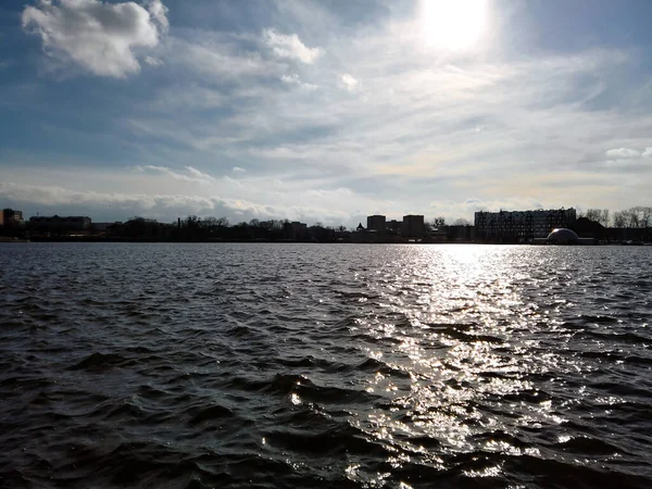 在俄罗斯加里宁格勒的一个阳光明媚的冬日里 城市池塘的堤岸上 波涛汹涌的水面上闪耀着太阳 高楼的轮廓映衬着现代城市景观 — 图库照片