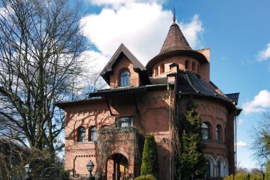 Güneşli bahar gününde Rusya 'nın Kaliningrad kentindeki (eski adıyla Koenigsberg) ağaç süsleme tesisleri tarafından döşenmiş kırmızı tuğla duvarlı ve bahçeli eski lüks evin ön cephesi