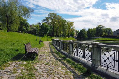 Kaliningrad, Rusya 'da güneşli bir bahar gününde kaldırımda boş ahşap banklar ve şehir göletinin kenarında yeşil çimenler bulunan kaldırımlar.