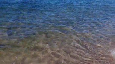 Sakin, berrak turkuaz su dalgalarının yakın çekimi güneşli yaz gününde Baltık kıyılarındaki kumsalın sığ kumları üzerinde yuvarlanıyor. İnsansız, sakin deniz manzaralı, doğal bir geçmişi var..