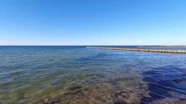 Güneşli bir yaz gününde berrak mavi gökyüzünün altında eski ahşap dalgalar üzerinde yuvarlanan durgun turkuaz dalgalarla Baltık deniz manzarası. Deniz manzarası yok, geniş açılı çekim..