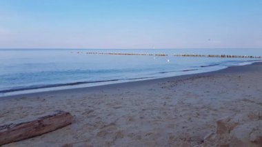 Serene seaside landscape with calm coastal surf water waves rolling on empty sand beach of Baltic sea shore under clear blue sky at cold cloudy morning. No people desolate seascape natural background.