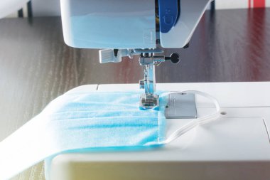 Dikiş makinesi evde dikişli tıbbi yeniden kullanılabilir koruyucu maske ile evde dikiş makinesiyle pamuk kumaş tıbbi maske yapıyor. Coronavirus pandemia Covid-19 virüs koruması. Seçici odak