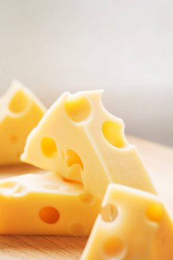 Tahta tabakta delikleri olan üç köşeli İsviçre peyniri parçaları. Maasdam Hollanda inek sütü peyniri