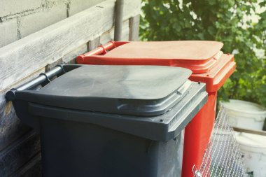 İki geri dönüşüm çöp kutusu kırmızı ve gri renkli. Renkli geri dönüşüm kutuları dışarıda. En az atık ayırma kavramı.