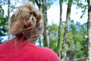 Sarışın beyaz kadın, saçları arkadan kıvırcık, ormana doğru bakıyor.