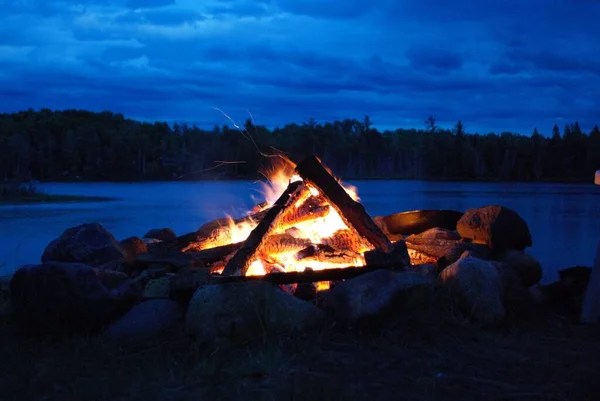 camp fire burning in a fire pit next to the lake