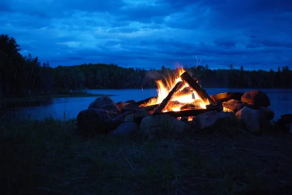 camp fire burning in a fire pit next to the lake