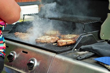 Arka bahçede ızgarada biftek pişiren kadın.