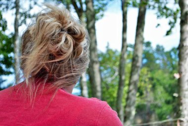 Sarışın beyaz kadın, saçları arkadan kıvırcık, ormana doğru bakıyor.