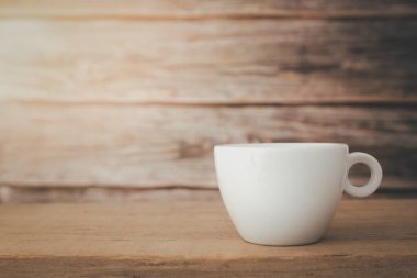 Tepesinden aşağı ışık saçan beyaz bir kahve fincanı ahşap bir tabağa ve ahşap bir zemin üzerine konur..